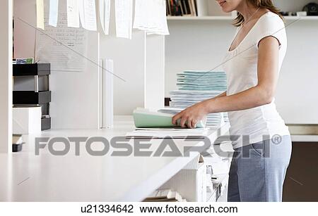 Stock Image - Office worker holding sorting paper materials standing in office. Fotosearch
