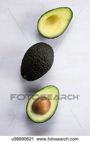 Stock Image - One avocado and another one cut in half. Fotosearch
