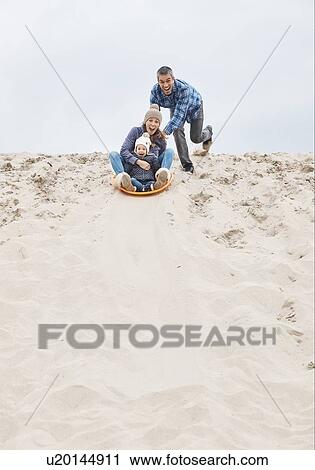 Stock Image - Parents and baby girl sand sledding on dunes. Fotosearch
