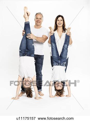 Stock Photo - Parents holding legs of children doing handstand, white background. Fotosearch