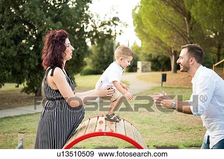 Stock Photo - Parents playing with son on circular swing in park. Fotosearch