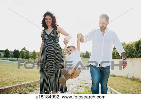 Stock Image - Parents swinging son by hands in park. Fotosearch