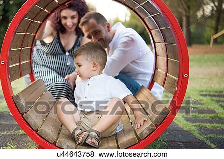 Parents watching son play in circular swing in park View Large Photo Image Stock Photo - Parents watching son play in circular swing in park. Fotosearch