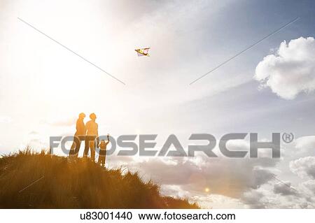 Stock Image - Parents with child playing with kite on the top of the hill. Fotosearch