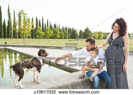 Stock Image - Parents with son playing with dog in park. Fotosearch