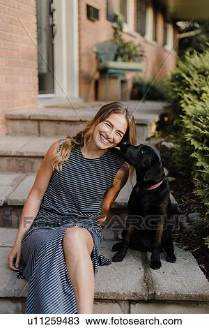 Stock Image - Pet dog licking woman on garden steps. Fotosearch