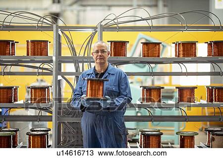 Stock Image - Portrait of electrical engineer with reel of copper wire in electrical engineering factory. Fotosearch