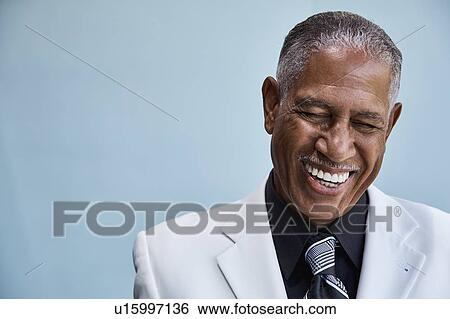 Stock Photograph - Portrait of senior businessman laughing, blue background. Fotosearch