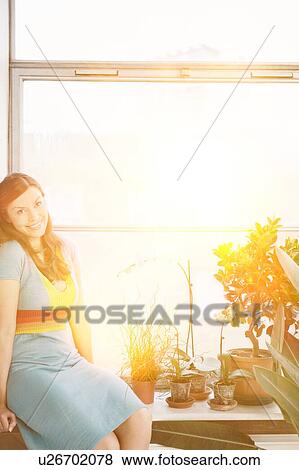 Portrait of young woman sitting on window sill at home View Large Photo Image Stock Photo - Portrait of young woman sitting on window sill at home. Fotosearch