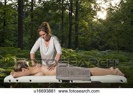 Stock Image - Professional masseuse treats woman on massage table in woods. Fotosearch