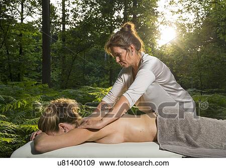 Stock Photo - Professional masseuse treats woman on massage table in woods. Fotosearch