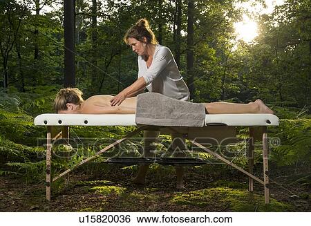 Stock Photograph - Professional masseuse treats woman on massage table in woods. Fotosearch