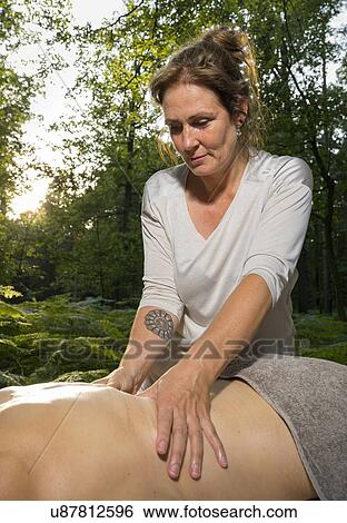 Stock Photograph - Professional masseuse treats woman on massage table in woods. Fotosearch