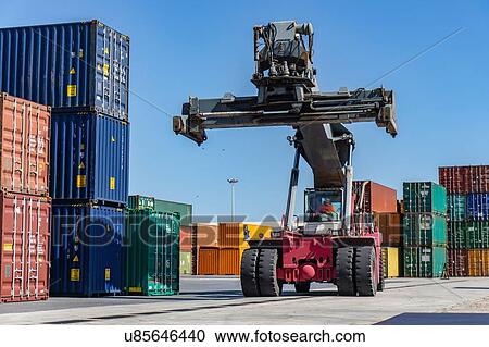 Stock Image - Reach stacker and shipping containers in dock. Fotosearch