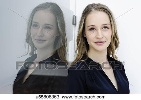 Stock Image - Reflection of young businesswoman leaning against glass wall. Fotosearch