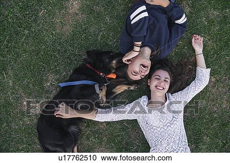 Stock Image - Sisters playing with dog in park. Fotosearch