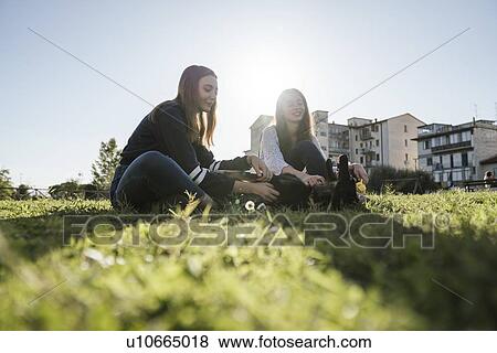 Stock Photo - Sisters playing with dog in park. Fotosearch