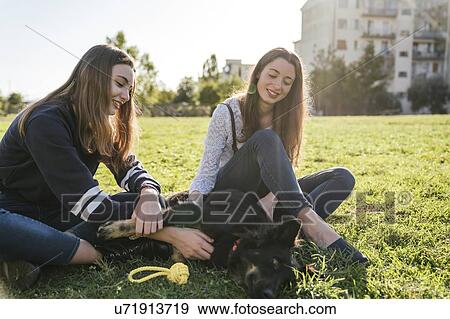 Stock Photo - Sisters playing with dog in park. Fotosearch