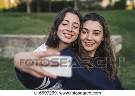 Stock Photo - Sisters taking selfie in park. Fotosearch