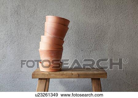 Stock Photo - Stack of plant pots on wooden stool, grey background. Fotosearch