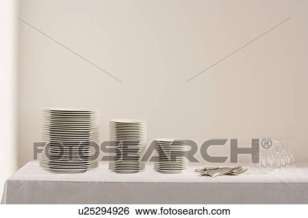 Stock Photograph - Stacks of plates cutlery and wineglasses on table. Fotosearch