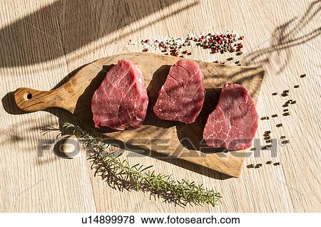 Stock Photo - Thick slices of raw meat, rosemary, peppercorn. Fotosearch