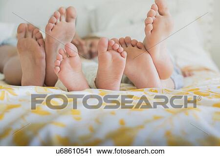 Stock Image - Three pairs of bare feet in a row, different sizes on a bed. Fotosearch