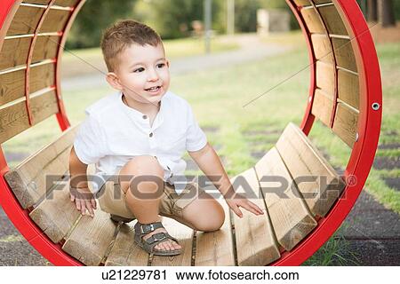 Stock Image - Toddler kneeling inside circular swing in park. Fotosearch