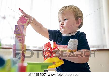 Toddler playing with building blocks in room View Large Photo Image Stock Photo - Toddler playing with building blocks in room. Fotosearch