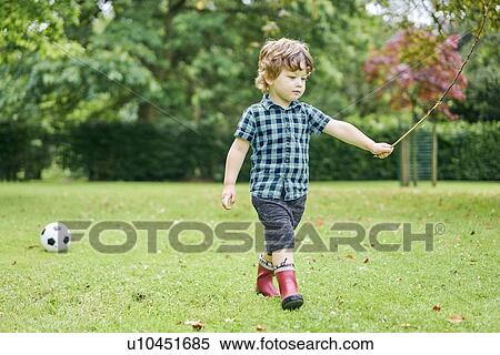 Stock Photography - Toddler playing with stick and football in park. Fotosearch