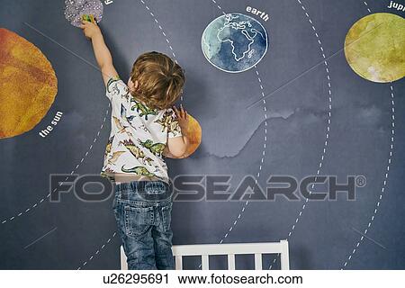 Stock Image - Toddler playing with toy on wall with mural of solar system. Fotosearch