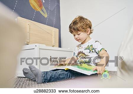 Stock Image - Toddler reading book in room. Fotosearch