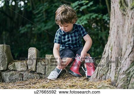 Stock Image - Toddler removing shoe beside tree. Fotosearch