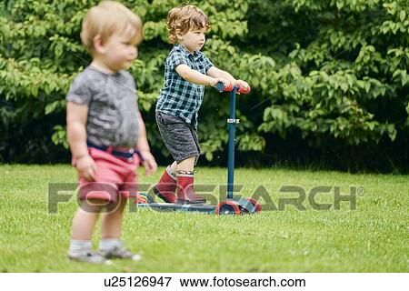 Toddlers exploring and riding push scooter in park View Large Photo Image Stock Photo - Toddlers exploring and riding push scooter in park. Fotosearch