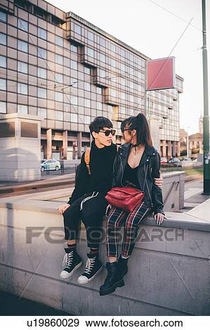 Stock Photo - Trendy couple sitting on concrete structure, Milan, Italy. Fotosearch