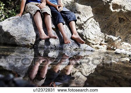 Two boys sitting on rock by river View Large Photo Image Stock Image - Two boys sitting on rock by river. Fotosearch