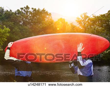 Stock Image - Two men carrying kayak outdoors. Fotosearch