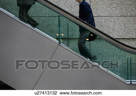 Stock Image - Two people going up escalator. Fotosearch