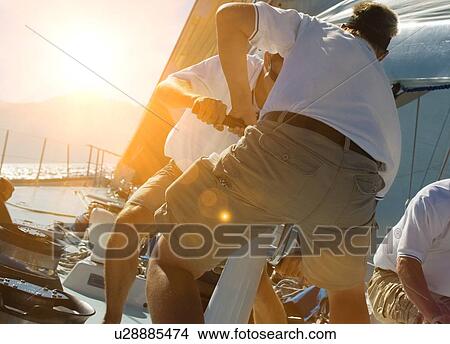 Picture - Two sailing crew members working rigging on sail boat with lens fare. Fotosearch