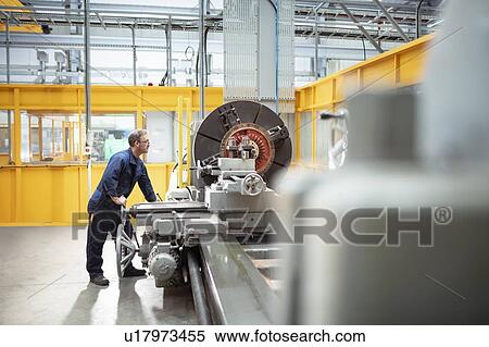 Stock Photography - Wide angle view of engineer operating lathe in electrical engineering factory. Fotosearch