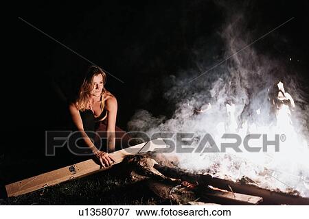 Stock Photo - Woman barbecuing over campfire at night. Fotosearch