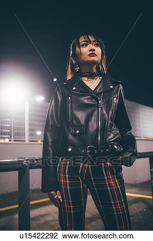 Stock Image - Woman beside railing, fencing and floodlights in background, Milan, Italy. Fotosearch