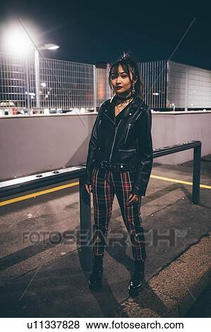 Stock Photo - Woman beside railing, fencing and floodlights in background, Milan, Italy. Fotosearch