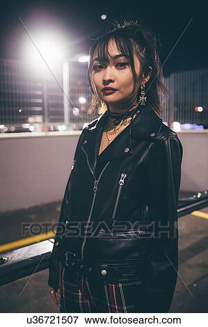 Stock Photo - Woman beside railing, fencing and floodlights in background, Milan, Italy. Fotosearch