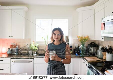 Stock Photo - Woman enjoying cup of hot beverage in kitchen. Fotosearch