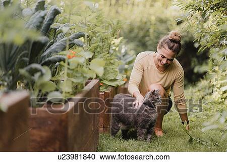 Stock Image - Woman gardener with cat in garden. Fotosearch