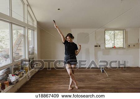 Woman holding paintbrush and dancing in new home View Large Photo Image Stock Photo - Woman holding paintbrush and dancing in new home. Fotosearch