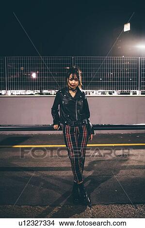 Picture - Woman leaning against railing, fencing and floodlights in background, Milan, Italy. Fotosearch