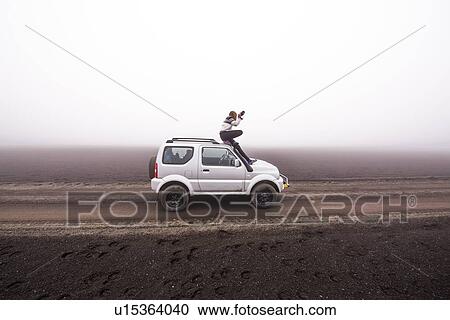 Stock Image - Woman photographing from top of off road vehicle, Landmannalaugar, Iceland. Fotosearch