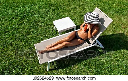 Stock Photo - Woman relaxing with mocktail in deckchair on lawn. Fotosearch
